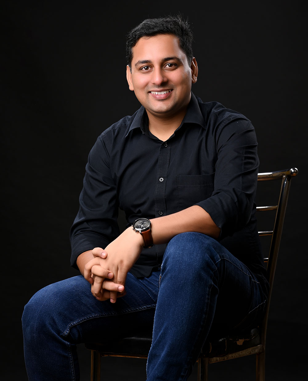 certified mindset Coach Rajendra in a black shirt, wearing a wristwatch, against dark background, radiating motivation