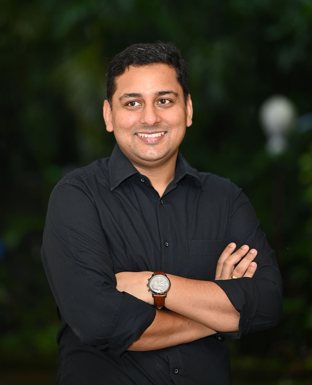 Coach Rajendra in a black shirt, with green foliage in the background, giving a friendly and motivational vibe