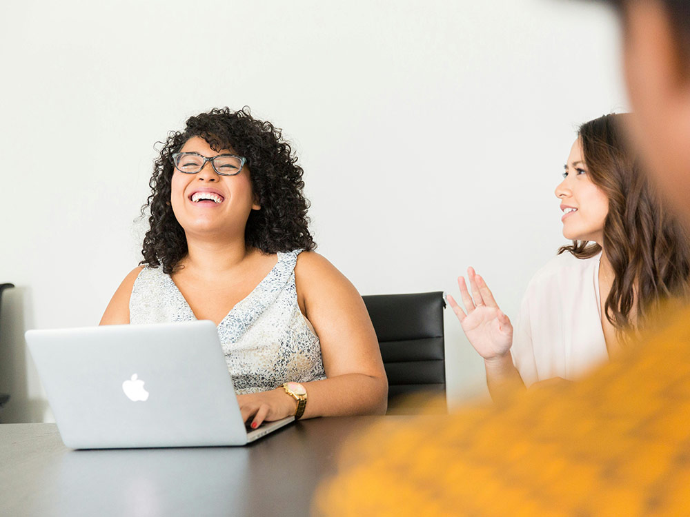 Two women engaged in mindfulness, sitting at a table with a laptop, fostering focus and connection in a serene environment