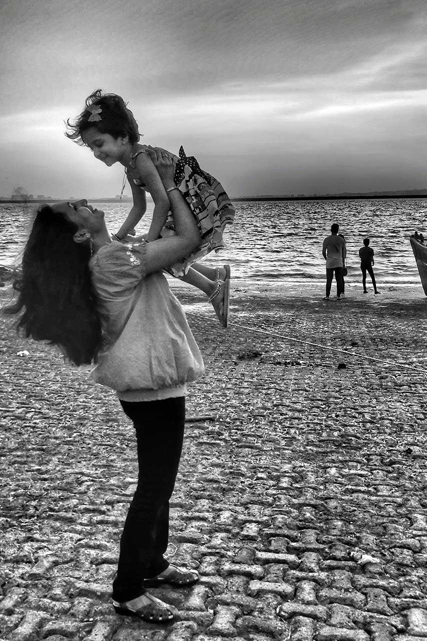  confident woman on beach holds her child, reflecting boundless spirit of working mother balancing career and family